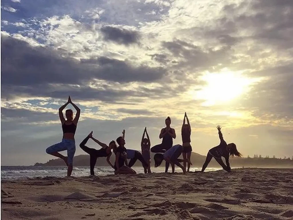 バイロンベイのビーチでサンセットを背景にヨガ