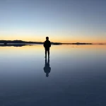 ウユニ塩湖の水鏡に立つ人物と夕焼けの空