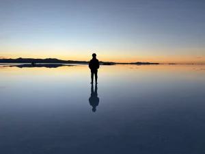 ウユニ塩湖の水鏡に立つ人物と夕焼けの空