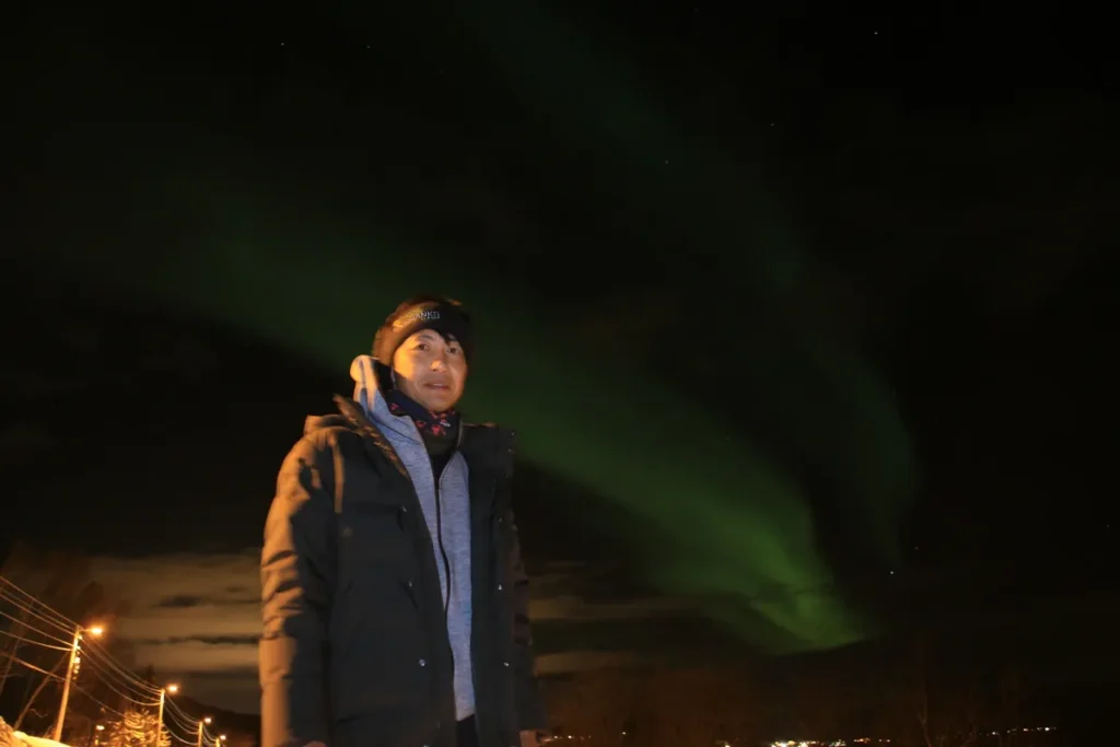 夜のオーロラの下で防寒着を着た旅行者が立つ冬の観測風景