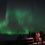 雪景色の観賞スポットでカップルが夜空に広がるオーロラを眺めている冬の旅行風景