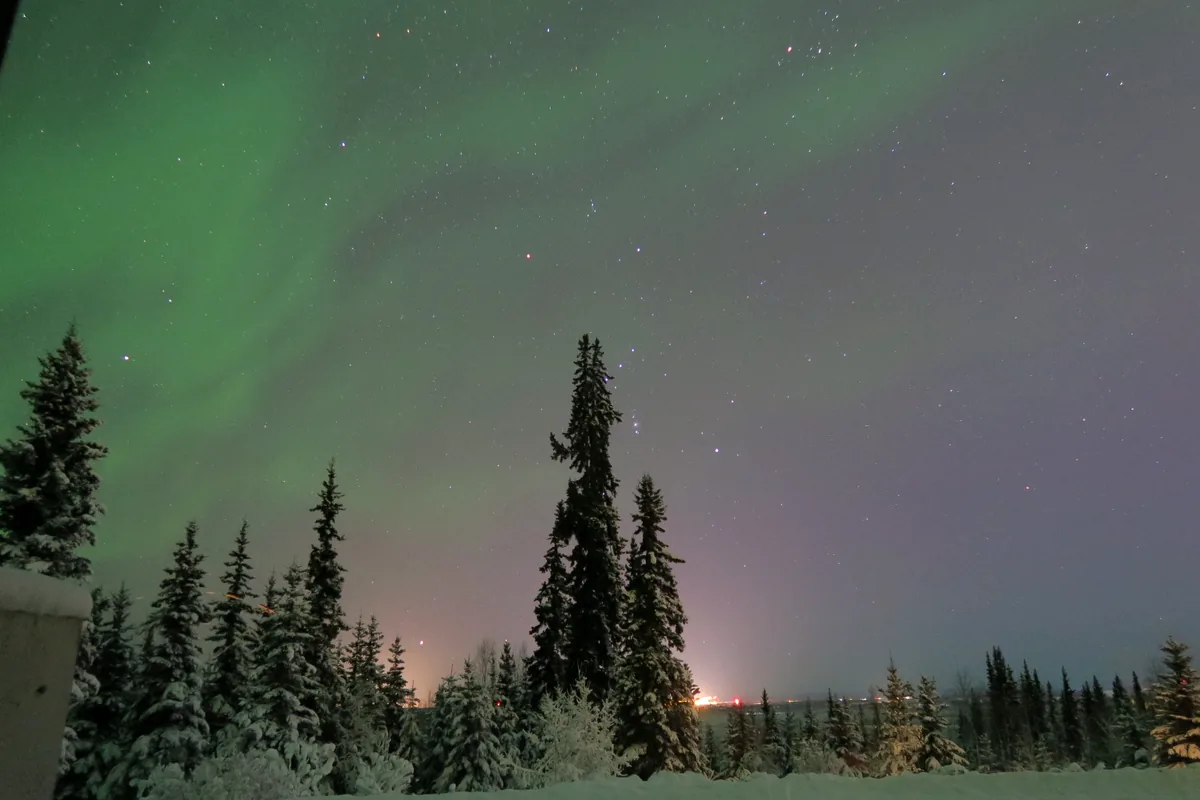フェアバンクスの雪の森に広がる淡いオーロラと星空の夜景