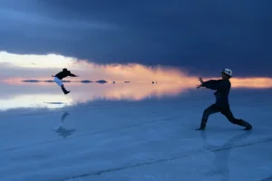 夕暮れのウユニ塩湖で遠近法のトリック写真を楽しむ旅行者2人の幻想的な風景