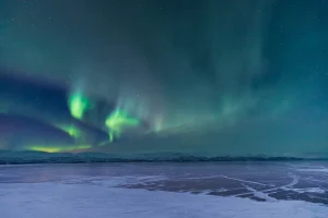 アビスコの凍った湖と雪山の上空に広がる緑のオーロラと星空