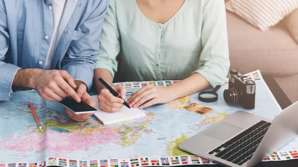 世界地図やPCを広げて旅行日程を相談するカップルのハネムーン計画イメージ