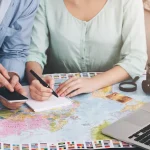 世界地図やPCを広げて旅行日程を相談するカップルのハネムーン計画イメージ
