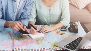 世界地図やPCを広げて旅行日程を相談するカップルのハネムーン計画イメージ