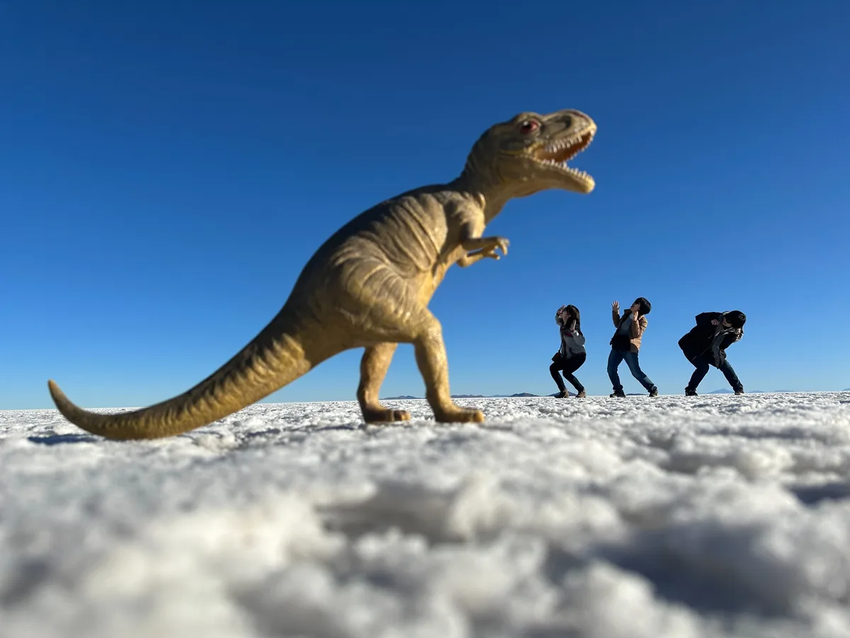 ウユニ塩湖で恐竜のフィギュアを使って遠近法撮影を楽しむ旅行者