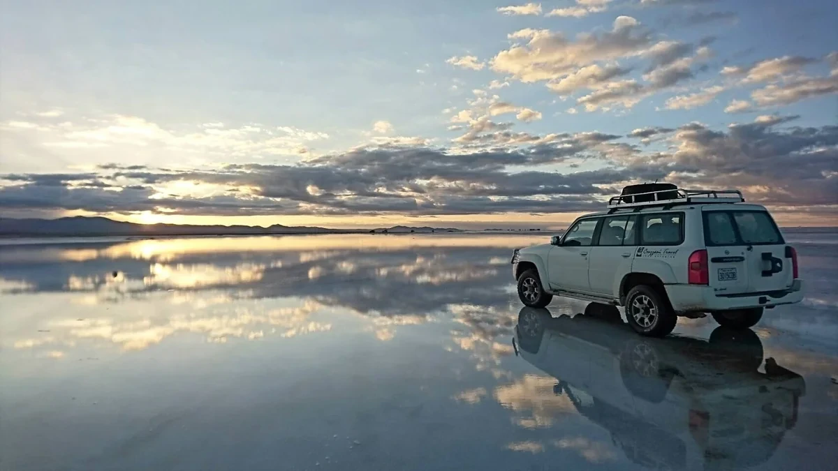 夕暮れのウユニ塩湖に空と雲が映り込み、車が停まる幻想的な風景