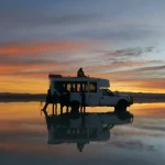 ウユニ塩湖の鏡張りに夕焼けと四駆ツアー車が映る南米旅行の風景
