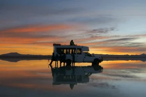 ウユニ塩湖の鏡張りに夕焼けと四駆ツアー車が映る南米旅行の風景
