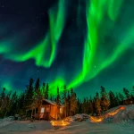 雪景色のロッジ上空に広がるオーロラと星空の風景