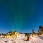 フィンランド・ラップランドの雪景色に建つガラスイグルーと夜空に広がるオーロラ