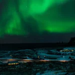 冬のアイスランドの海岸沿いに広がる雪景色と夜空を彩るオーロラ