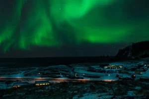冬のアイスランドの海岸沿いに広がる雪景色と夜空を彩るオーロラ