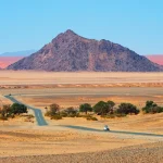 ナミビアの砂漠地帯を走るレンタカーと山々を望む長い一本道