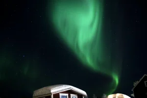 雪の積もったキャビンの上空に広がる緑のオーロラ