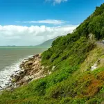 ケアンズ近郊の海岸沿いを走る車と青い海、緑豊かな山並みが広がるドライブ風景