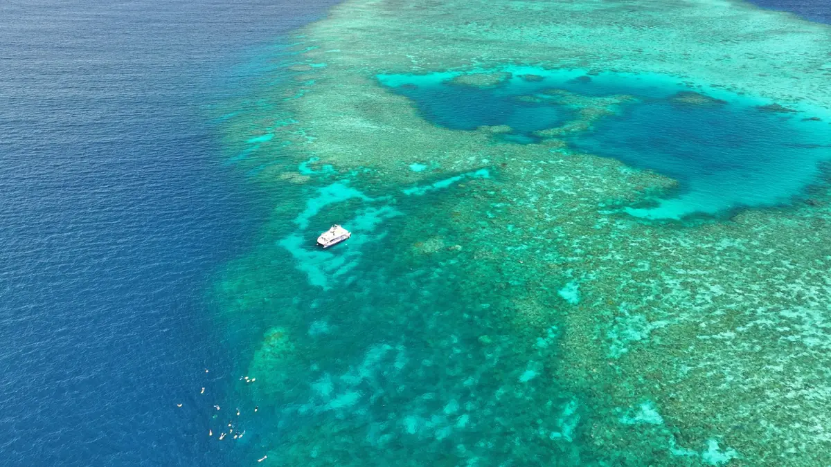 上空から見渡すターコイズブルーの浅瀬と広大なサンゴ礁、その近くに浮かぶ白い船