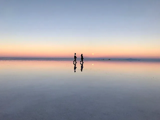 夕空を映すウユニ塩湖と二人の人影