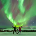 雪景色の中でオーロラを楽しむ2人の旅行者