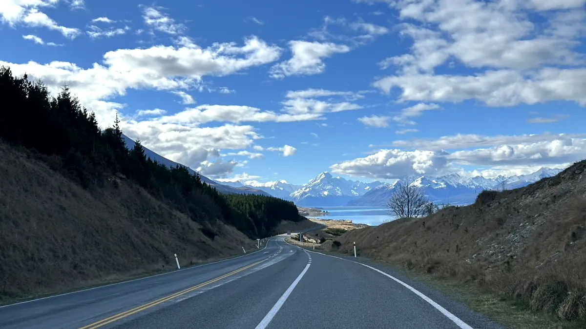 南島の道路の先に広がる青い湖と雪山の連峰