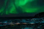 冬のアイスランドの海岸沿いに広がる雪景色と夜空を彩るオーロラ